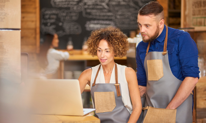 A business owner and employee in a cafe look at a laptop