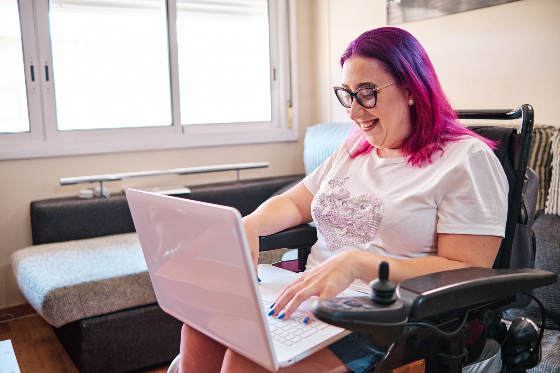 A smiling woman seated in a motorized wheelchair working on a laptop