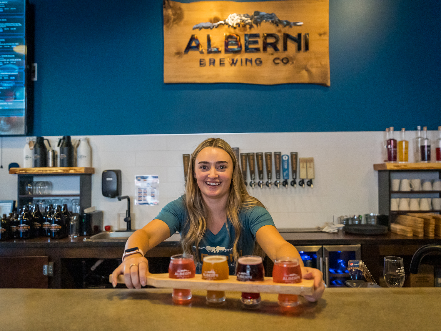 A smiling woman presents a flight of beer at Alberni Brewing Co. in Port Alberni